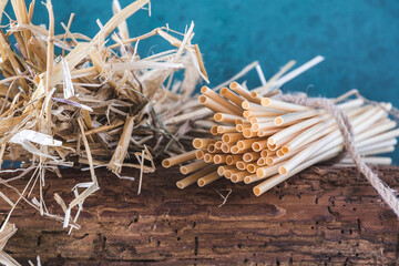 Natural straw drinking straws and a bundle of straw on an old wooden beam, blue background. Concept...