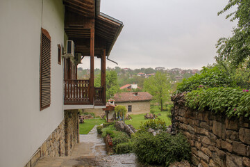 View from the hill to the white house with carved wooden balconies with running water on the stone pavement and standing in the distance stone houses