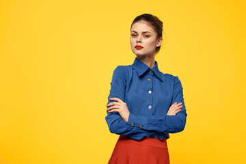 Attractive woman in blue shirt gesturing with her hands and red skirt yellow background portrait cropped view