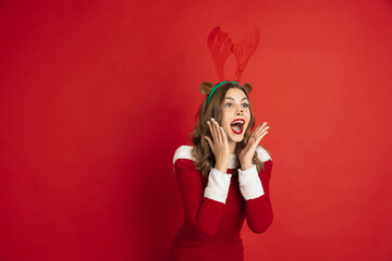 Shocked. Greetingcard. Concept of Christmas, 2021 New Year's, winter mood, holidays. Copyspace for ad, postcard. Beautiful caucasian woman with long hair like Santa's Reindeer catching giftbox.