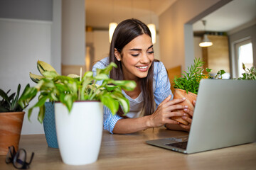Portrait of young smiling woman in a beige apron watching You tube tutorial on a laptop and...