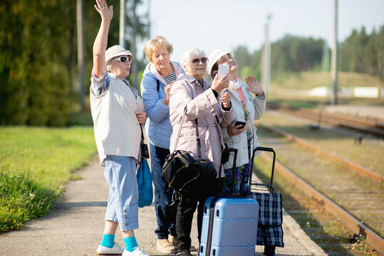 Group of smiling senior women take a self-portrait on a platform waiting for a train to travel during a COVID-19 pandemic