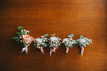 Top view of elegant handmade wedding boutonnieres in pastel colors on a wooden lacquered table.