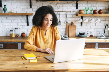 Beautiful multi-ethnic woman using laptop for work at home office . A girl with an afro hairstyle is typing on keyboard answering email. Remote work concept