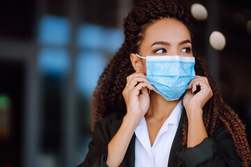 Portrait of brunette woman in protective sterile medical mask on her face looking at camera outdoors close up. Health protection, safety and pandemic concept. Covid - 19.