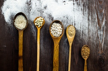 Top view of wooden spoons on which lie different cereals on a table sprinkled with flour.