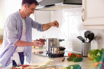 Smiling man salting broth on kitchen