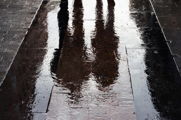 Sombra de un pareja reflejada en el suelo mojado de una calle por la lluvia