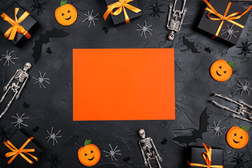 Halloween holiday background with blank orange card surrounded by gifts and decorations on black backdrop.