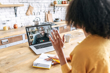 Back view african american woman talks via video with a black male colleague on the laptop screen. Virtual morning meeting, remote work from home