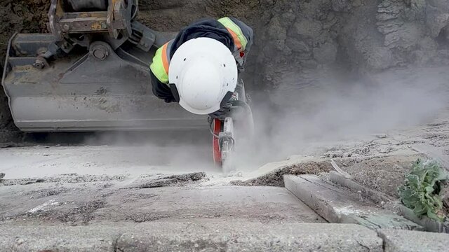 Slow motion of a man cutting cement with a concrete saw.  Lots of dust.  Safety and Danger very present.