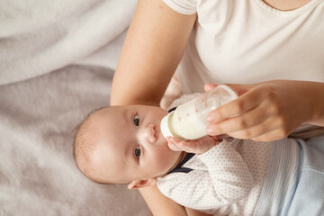 baby eats milk from a bottle and looks at camera