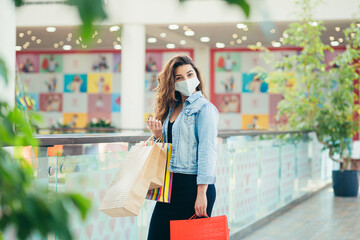 Happy young woman in medical mask walking at mall with lots of shopping bags in hands. Concept of healthcare and prevention from coronavirus.