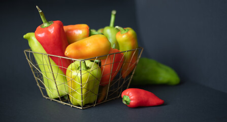 A large bowl of fresh bell peppers of different sizes and colors on a black background. Top view.