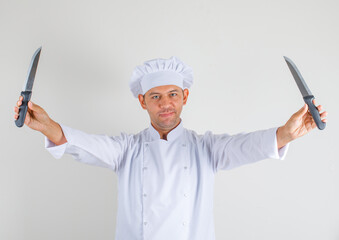 Male chef cook holding knives and smiling in hat and uniform , front view.