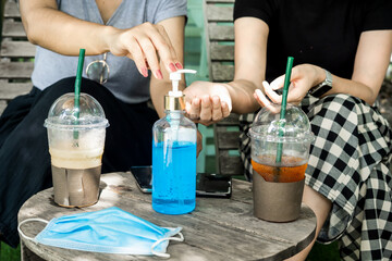 two female customers cleaning their hand  with alcohol gel at coffee shop, new normal concept
