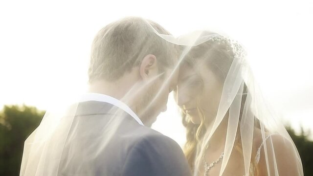 A groom kisses his bride's forehead while they pose for a photo under her veil