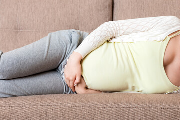 Beautiful pregnant woman suffering belly ache lying on a sofa at home