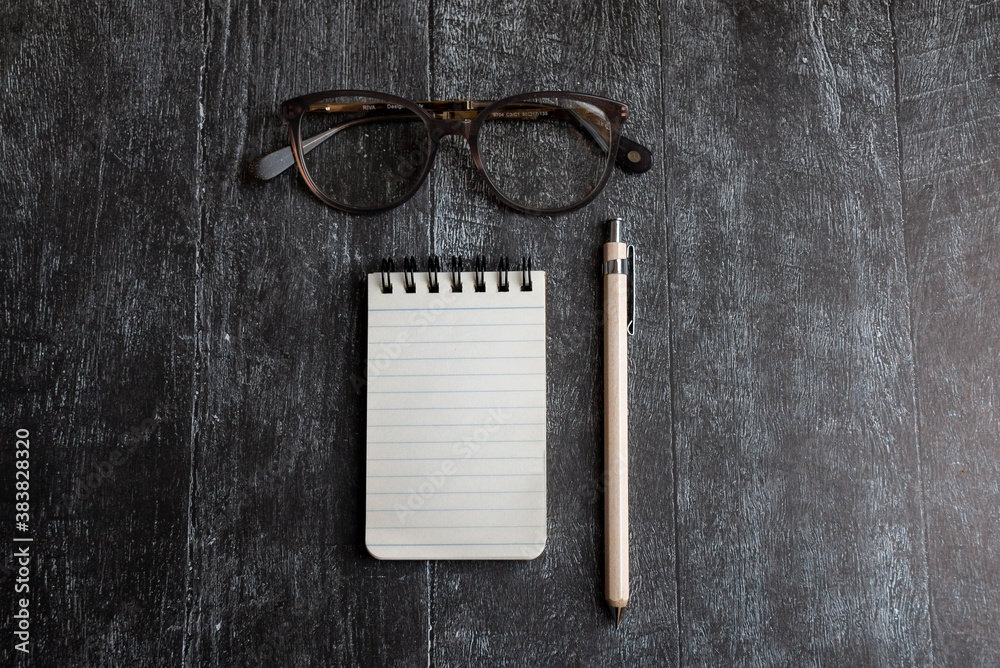 Wall mural staionery scene. open notebook pencil and stylish glasses on black wooden background. flat lay top view