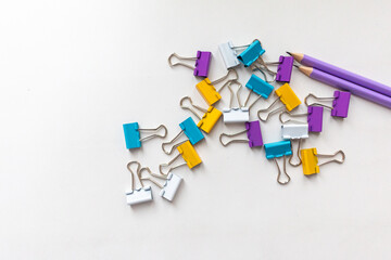 colorful paper clips amd purple pencils on white background. Stationery scene.