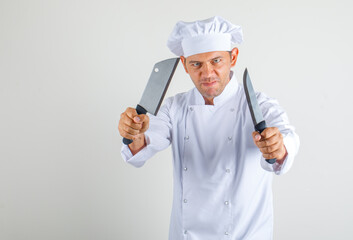 Male chef cook holding kitchen knives in uniform and hat and looking confident. front view.