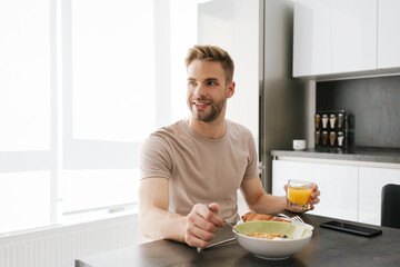 Fototapeta na wymiar Young handsome man smiling while having breakfast at home