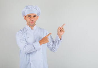Male chef cook in hat and uniform pointing fingers at something and looking confident , front view.