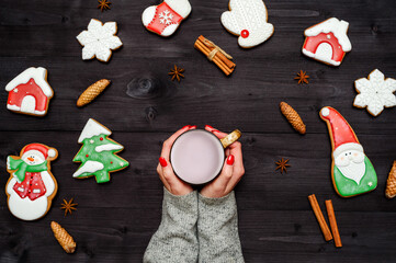 Woman with red manicure holding in hands cup of hot cocoa, copy space. Christmas background with gingerbread cookies, cinnamon and pine cones on dark wood desk. Top view, flat lay