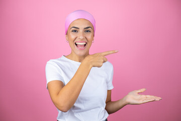 Young beautiful woman wearing pink headscarf over isolated pink background surprised, showing and pointing something that is on her hand