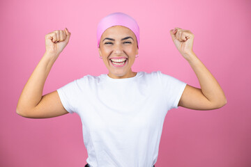 Young beautiful woman wearing pink headscarf over isolated pink background very happy and excited making winner gesture with raised arms, smiling and screaming for success.