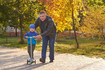 Dad teaches his two-year-old son to ride a scooter.