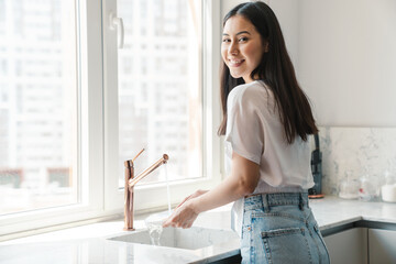 Positive young woman at home washing the dishes