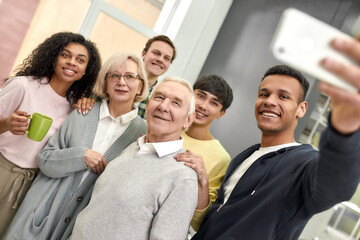 Obraz premium Happy young team smiling while taking selfie with aged man and woman, senior interns, Greeting new employees in the modern office