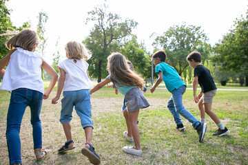 Group of active kids having race in park, running on grass together. Back view. Children outdoor...