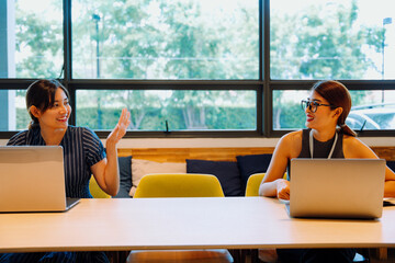 Two business women working together with laptop computer in co-working space.