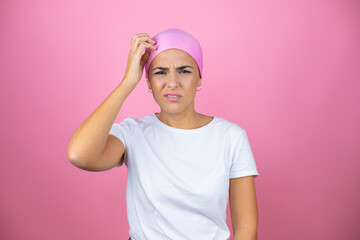 Young beautiful woman wearing pink headscarf over isolated pink background confuse and wonder about question. Uncertain with doubt, thinking with hand on head