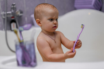 A little girl brushes her teeth in a lilac bathroom. Next to it is a glass.