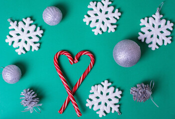 Heart shape with red Christmas candy canes, white large snowflakes, silvery balls on a green background, top view