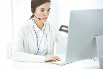 Call center. Casual dressed woman sitting in headset at customer service office. Group of operators at work. Business concept