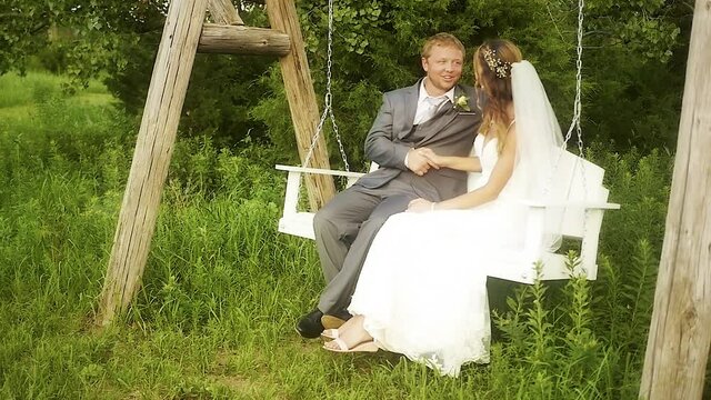 A bride and groom shaking hands while sitting on a white bench swing