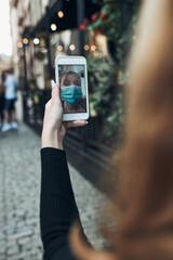 Young woman having video call talking while walking downtown in the evening wearing the face mask to avoid virus infection and to prevent the spread of disease in time of coronavirus