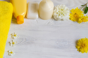 Composition of bath accessories in yellow and white colors: towel, soap, shampoo, flowers, aroma candle. Background. Copy space.