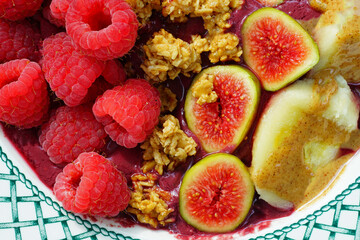 View of an acai bowl with fresh figs, raspberries, banana and granola
