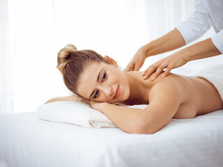 Fototapeta na wymiar Young and blonde woman enjoying massage of back in spa salon. Beauty concept