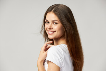 Fototapeta premium A woman with long hair smiles on a light background and touches her neck with her hands