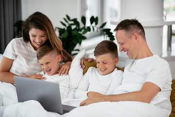 Beautiful parents with kids enjoying at home. Young family watching movie on lap top.