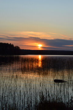 Sunset on the lake. Strong, beautiful colours, clouds and darkening evening. reflection from water and waterplants © Heli