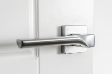 The silver metal doorknob is mounted in a white wooden door