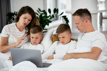 Beautiful parents with kids enjoying at home. Young family watching movie on lap top.