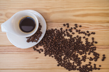 Cup of coffee  with scattered coffee beans on light  wooden  table